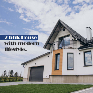 Exterior view of a modern 2 BHK house with a grey and white facade and a well-maintained lawn.