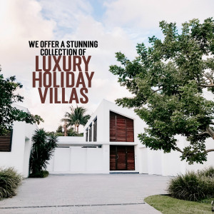 Modern white villa with lush greenery and a driveway, advertising luxury holiday rentals.