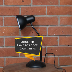 Black desk lamp with a sign promoting soft light, placed on a wooden surface against a brick wall.