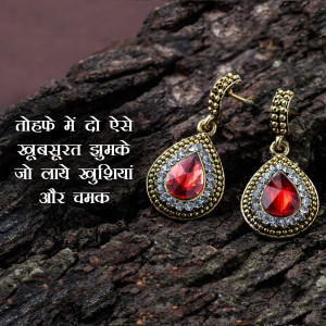 Close-up of ornate gold earrings with red gemstones on a textured wooden background.