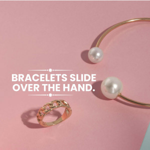 Close-up of gold bracelets and a ring on a pink background