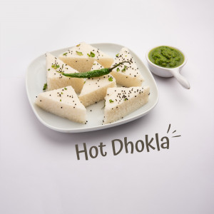 A plate of triangular steamed dhokla garnished with black sesame seeds and a green chili, served with green chutney.