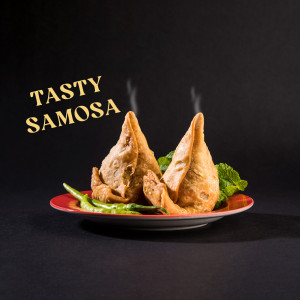 Two golden-brown samosas on a red plate with green chili and mint leaves.