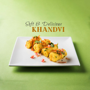 A plate of Khandvi, a traditional Gujarati snack, garnished with coriander and pomegranate seeds.