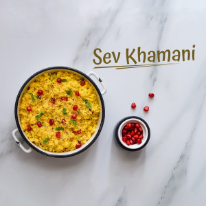 Top-down view of a bowl of Sev Khamani garnished with pomegranate seeds and cilantro, served with a side of pomegranate seeds.