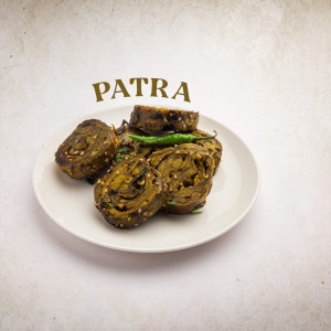 Close-up of Patra, a traditional Gujarati snack, served on a white plate with a green chili.