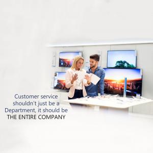 A couple looking at a tablet in front of a display of televisions in a store.