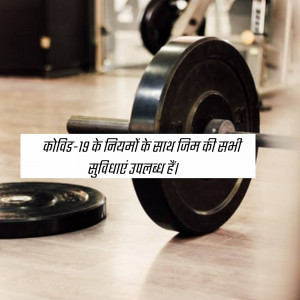 Weight plates on the floor in a gym with a sign about COVID-19 safety measures.