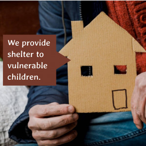 Hands holding a cardboard house with text 'We provide shelter to vulnerable children.'