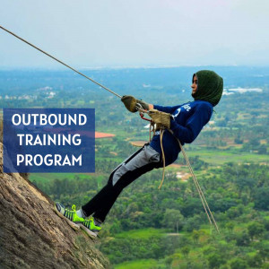 A woman in a hijab rappelling down a rocky cliff during an outbound training program.
