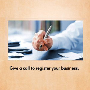 Hand holding a pen over paperwork with a phone in the background and text encouraging business registration.
