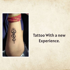 Close-up of a black trident tattoo on a person's wrist with a red bracelet.