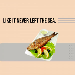 A close-up of a grilled fish served with lemon, olives, and a side of sauce on a white plate.