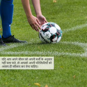 Close-up of a soccer ball on a green field with a player preparing to kick it.