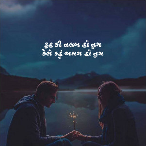A couple sitting close together holding a sparkler with a mountain and lake backdrop.