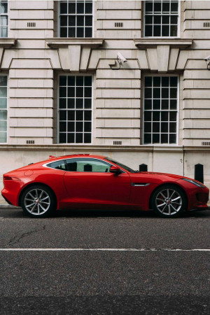 A red Jaguar sports car parked on a city street with a building in the background.