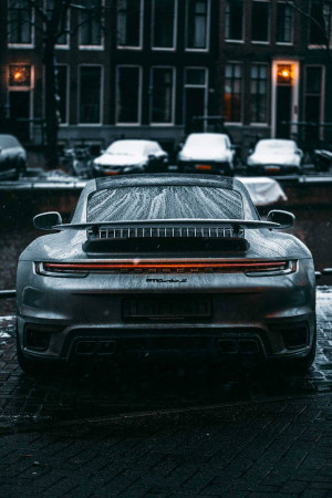 Rear view of a silver Porsche 911 parked on a wet cobblestone street at night.