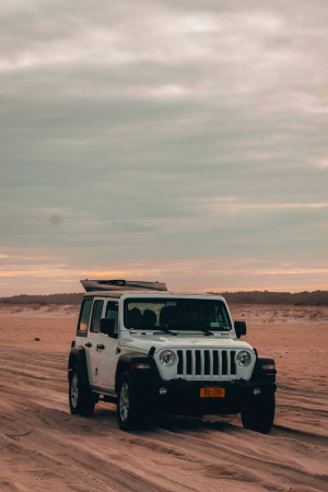 White Jeep Wrangler parked on a sandy desert road at sunset