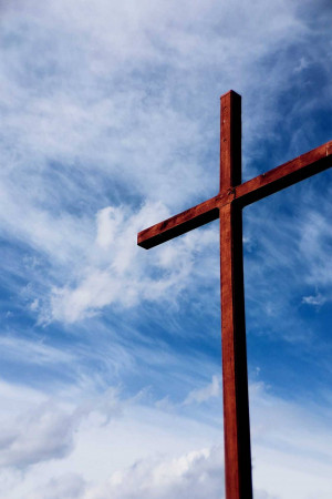 Wooden cross silhouetted against a bright blue sky with fluffy clouds