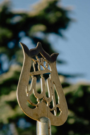 Close-up of a golden Islamic calligraphy symbol against a blurred green background.