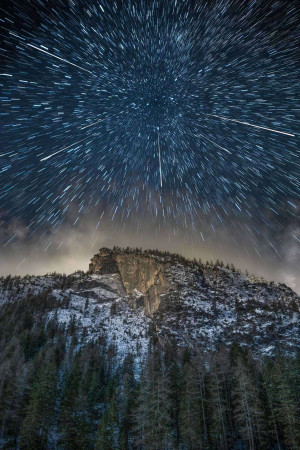 Long exposure photograph of a star trail over a mountain range.