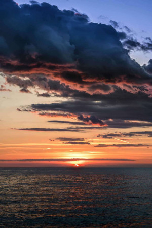 Sunset over the ocean with dark, dramatic clouds