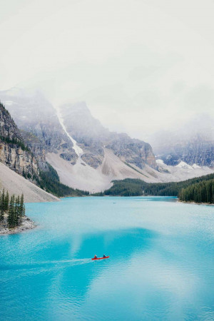 Two kayakers on the turquoise waters of Moraine Lake, surrounded by mountains.