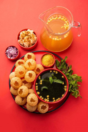 A vibrant overhead shot of Pani Puri, a popular Indian street food, with all its components arranged on a red background.