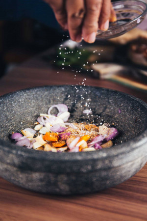 Close-up of hands seasoning chopped onions and garlic in a stone mortar with a grater.