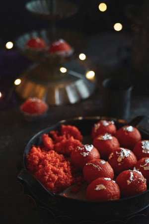 Close-up of traditional Indian sweets like Gulab Jamun and Besan Ladoo arranged on decorative trays with blurred lights in the background.
