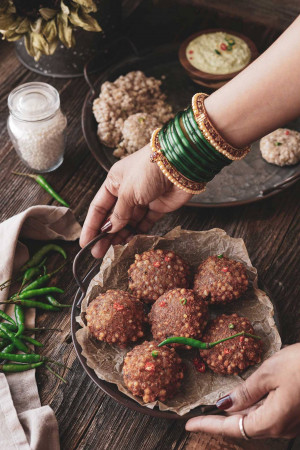 Close-up of a hand reaching for Rava Idli served with green chutney and spices.