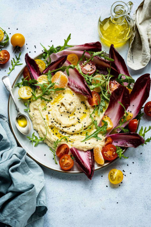 Overhead shot of a beautifully plated hummus dish with tomatoes, radicchio, and citrus fruits.