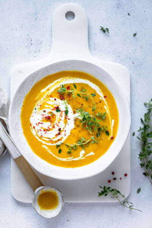 Overhead shot of butternut squash soup in a white bowl on a white wooden board.