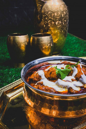 Close-up of a bowl of Butter Chicken with golden accents and a decorative background.
