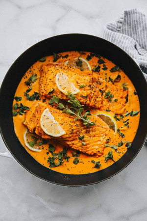 Overhead shot of salmon fillets in a creamy Tuscan sauce with lemon slices and herbs.