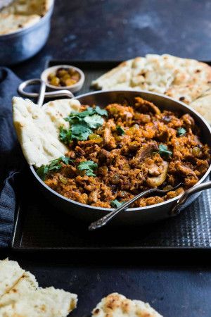 Close-up of a flavorful lamb curry served with naan bread and fresh cilantro.