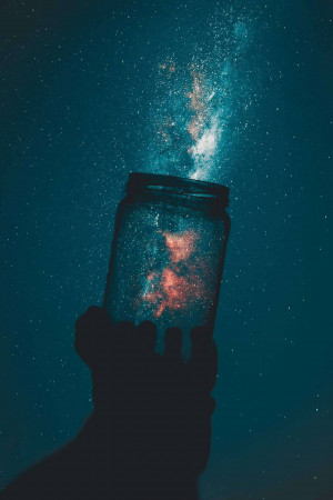 Silhouette of a hand holding a jar filled with a galaxy