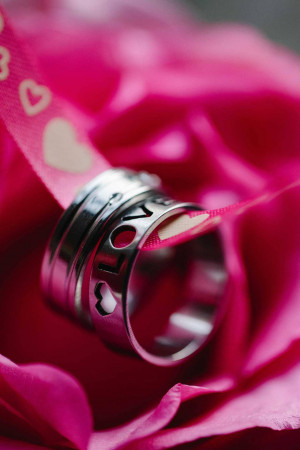 Close-up of a wedding ring with the word 'LOVE' engraved on it, resting on a pink rose.
