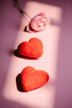 Close-up of red velvet hearts and a pink rose on a pink background with dramatic lighting.