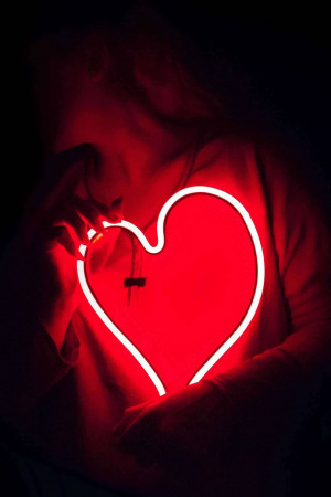 Person holding a glowing neon heart shape in the dark