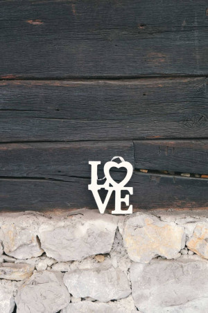 White 'LOVE' sign hanging on a rustic wooden wall with a stone base.