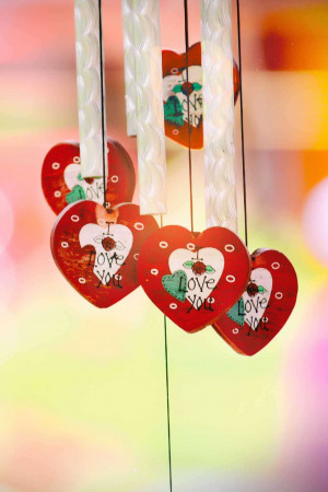 Close-up of a wind chime with red heart-shaped pendants that say 'I Love You'.