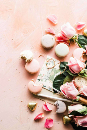 Flat lay of pink macarons, roses, and stationery on a pink background