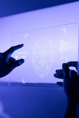 Hands interacting with a transparent screen displaying a facial recognition scan.