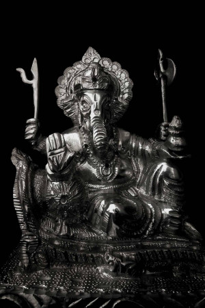 Close-up of a silver-colored Ganesha statue against a black background