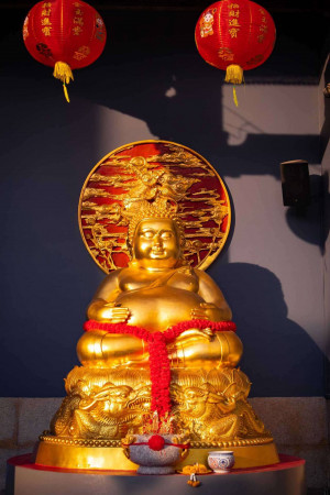A golden statue of a smiling Buddha with red lanterns hanging above.
