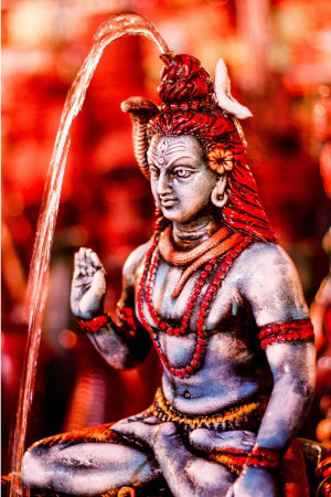 Close-up of a silver-colored statue of Lord Shiva with water cascading down, adorned with red flowers and beads.