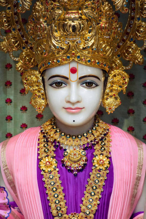 Close-up of a marble Swaminarayan idol adorned with gold jewelry and a floral garland.