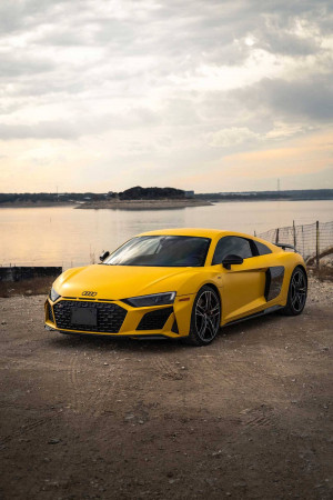 A vibrant yellow Audi R8 sports car parked near a lake.