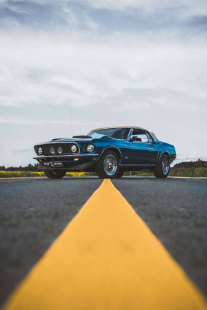 A blue 1967 Ford Mustang parked on a road with a yellow center line.